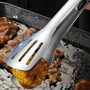 Stainless steel grilling tongs holding corn and meat on a hot flat-top grill