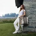 Woman in white linen outfit leaning against a stone wall outdoors, carrying a large boho-style woven tote bag