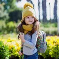 oung girl wearing a yellow knit hat and scarf, carrying a floral backpack, ready for back to school