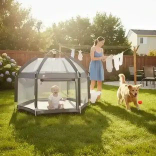 Baby sitting in an outdoor mesh playpen on a sunny backyard lawn while a mother hangs laundry and a golden dog plays nearby