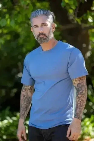 Middle-aged man with silver hair, beard, and tattoo sleeves wearing a blue crew-neck t-shirt