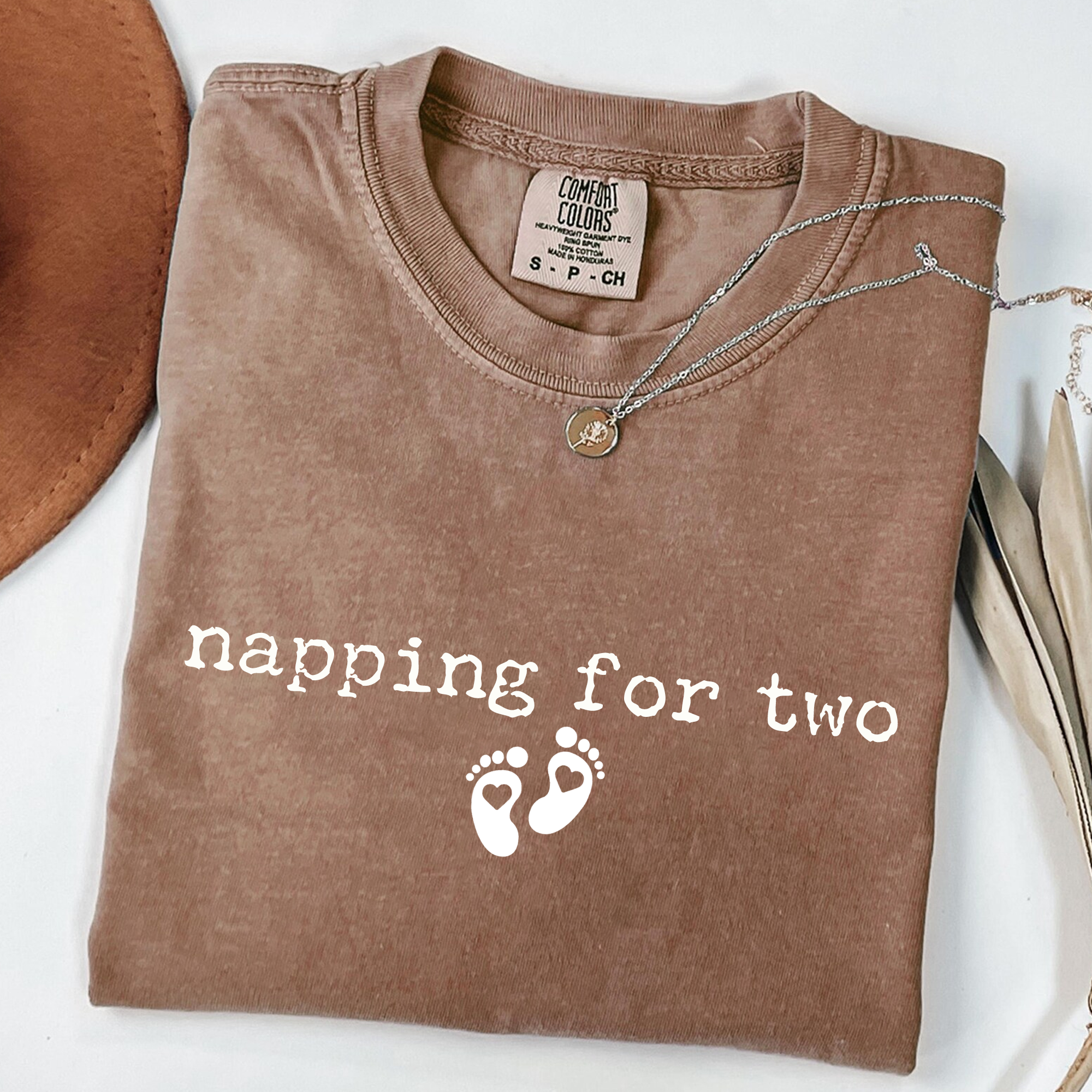 Brown t-shirt with 'napping for two' text and footprints on a white surface