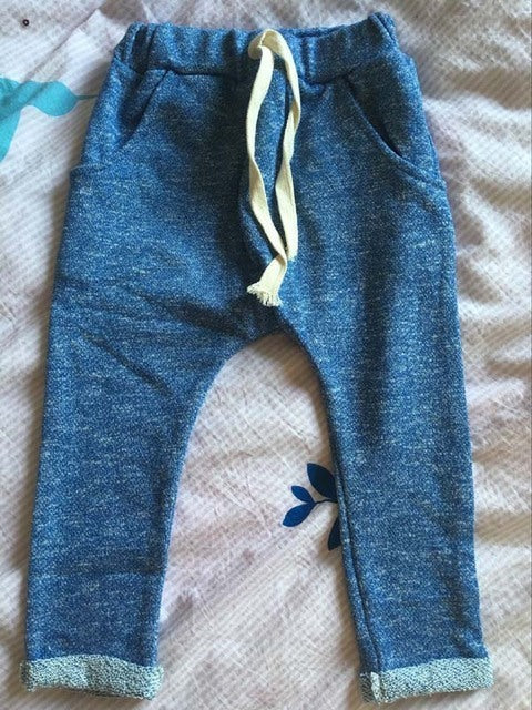 Blue children's pants with a yellow drawstring on a patterned surface