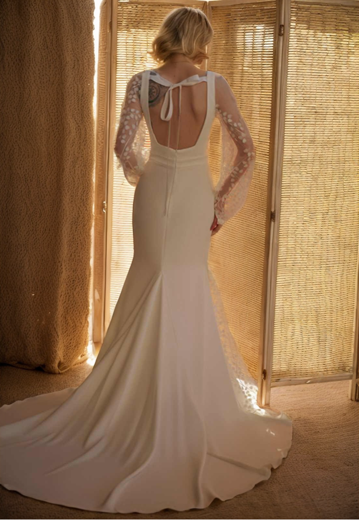 Woman in a white wedding dress with lace sleeves standing in front of a textured wall.
