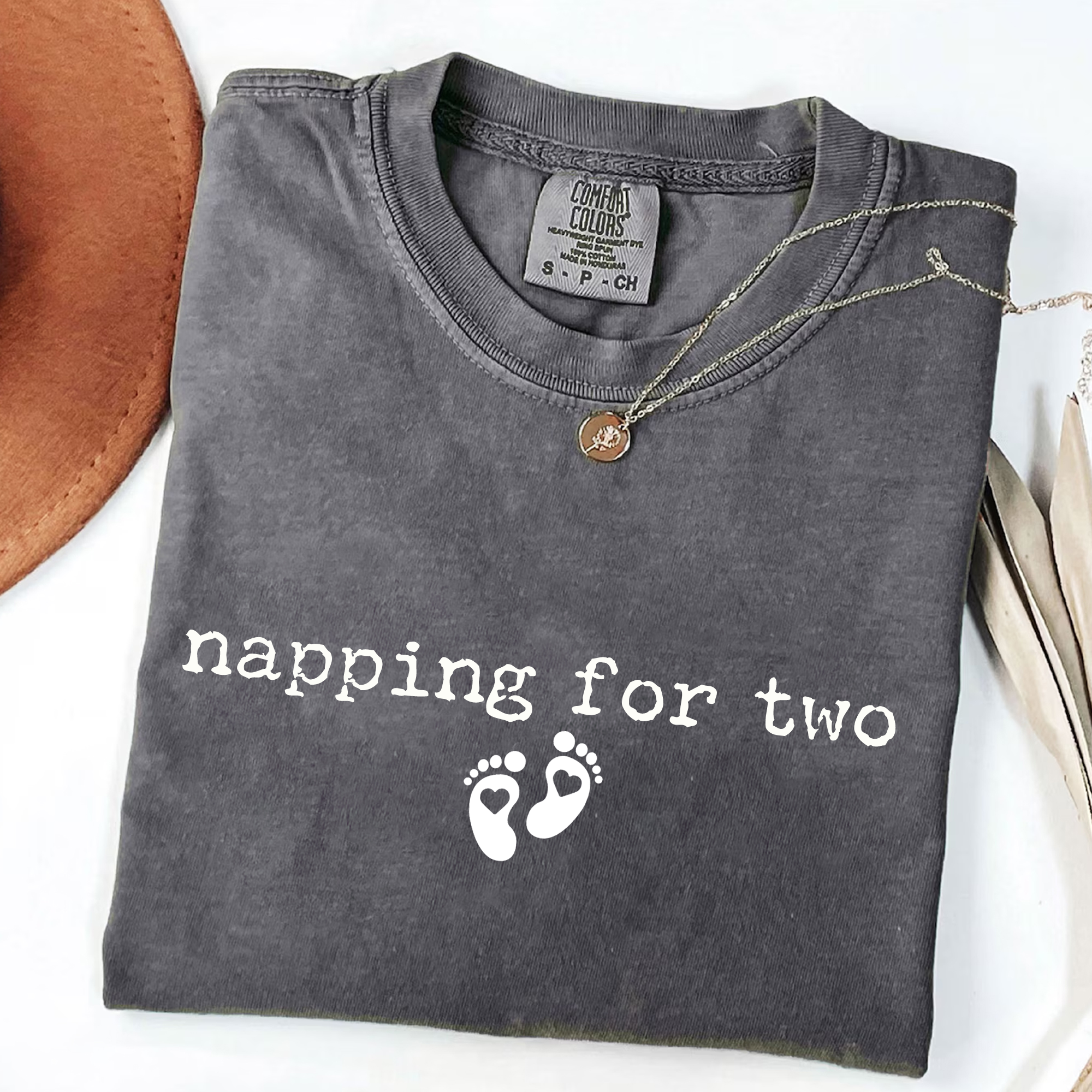 Folded gray t-shirt with 'napping for two' text and footprints on a white background