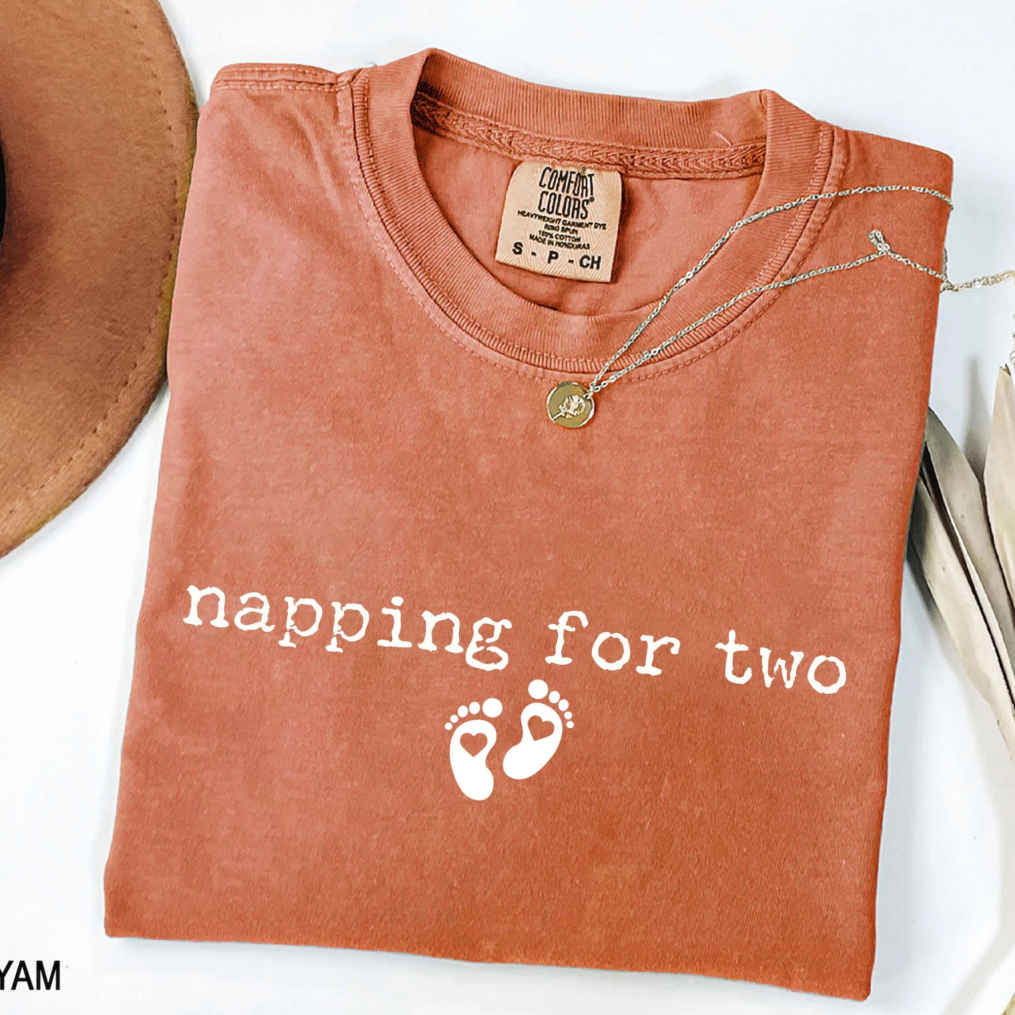Folded orange t-shirt with 'napping for two' text and footprints on a white background