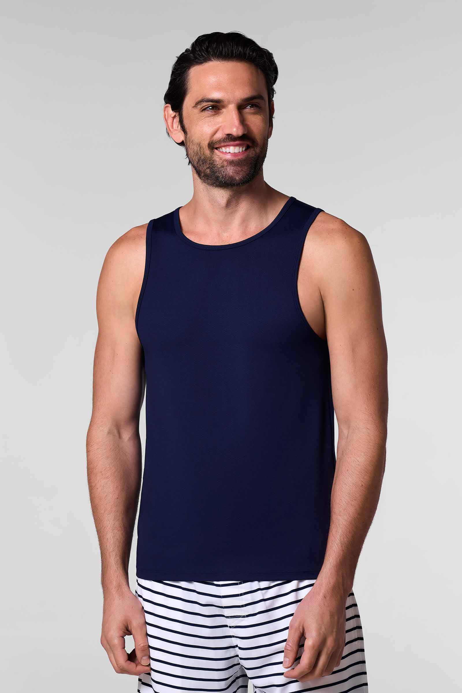Man wearing a navy tank top and striped shorts on a plain background