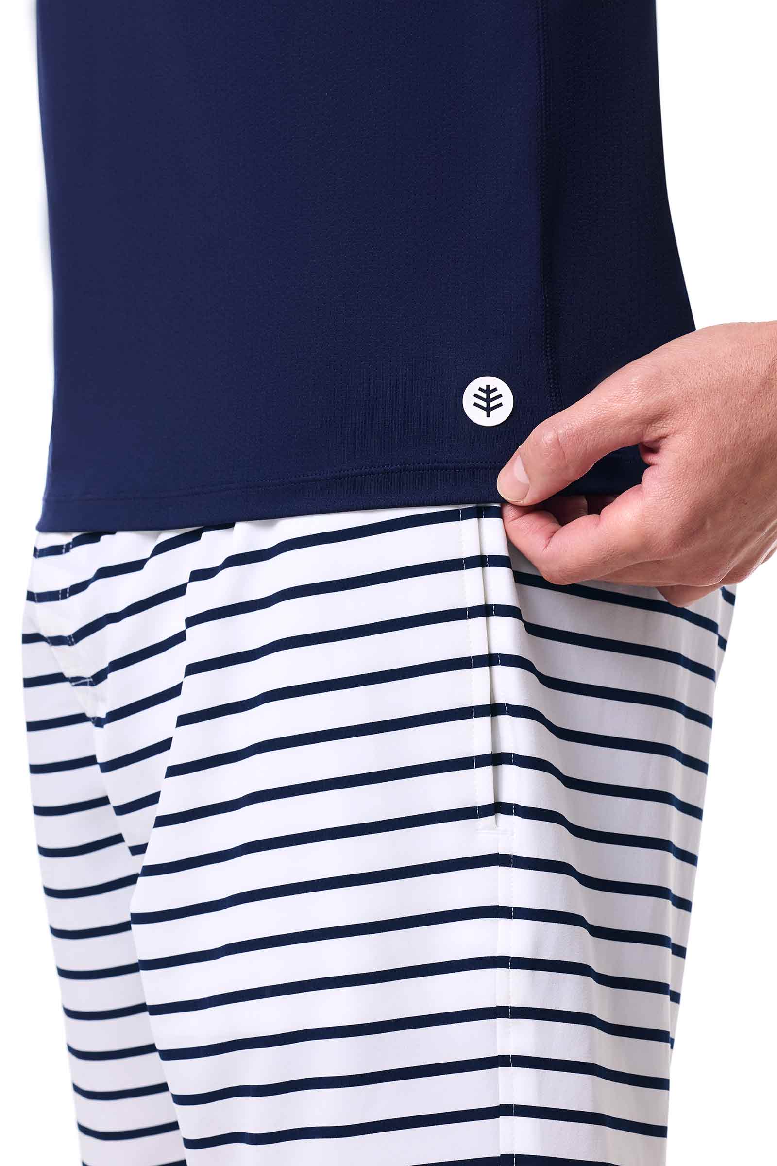 Navy blue top and white striped pants with a hand adjusting the waistband on a white background