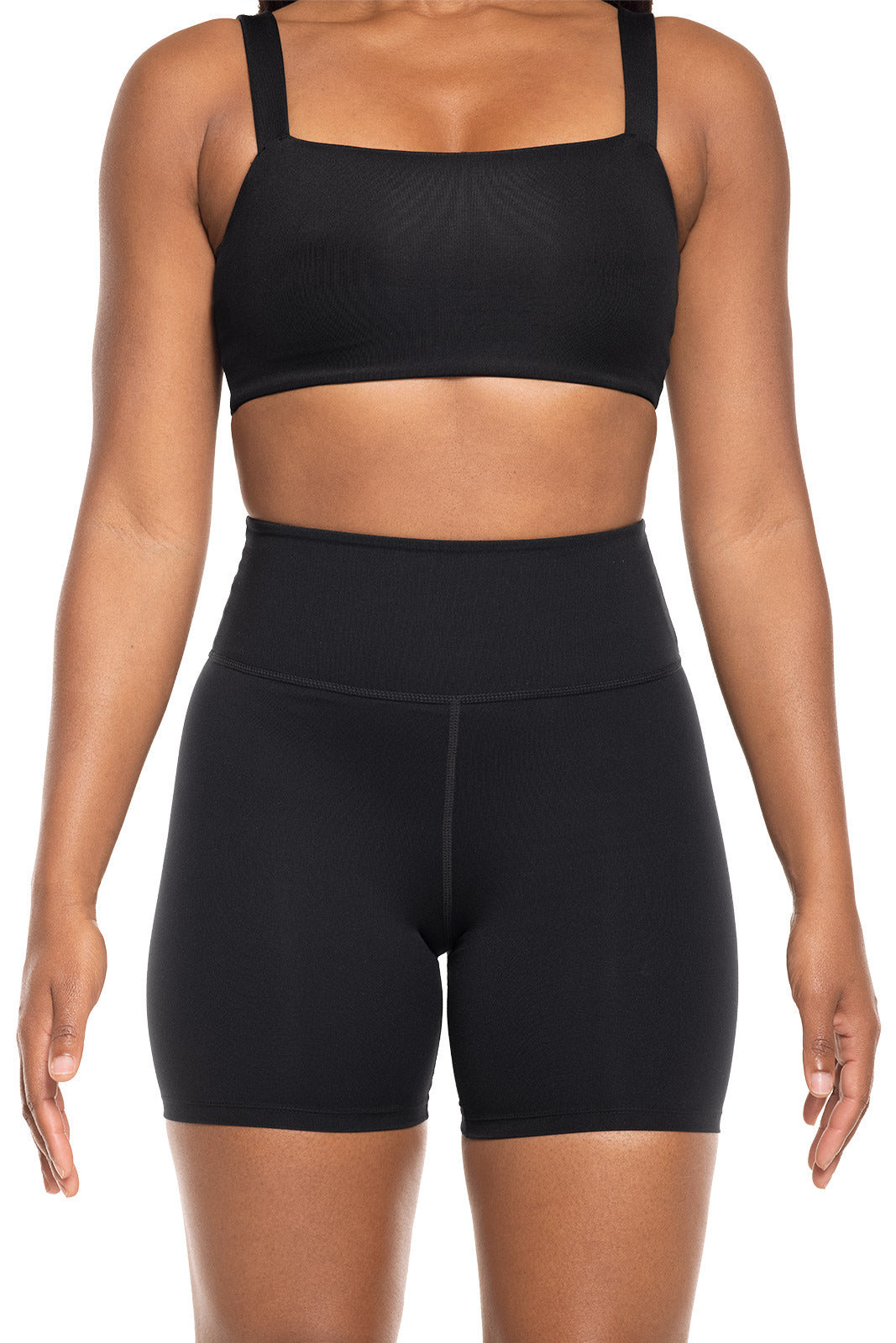 Person wearing a black sports bra and high-waisted shorts on a white background