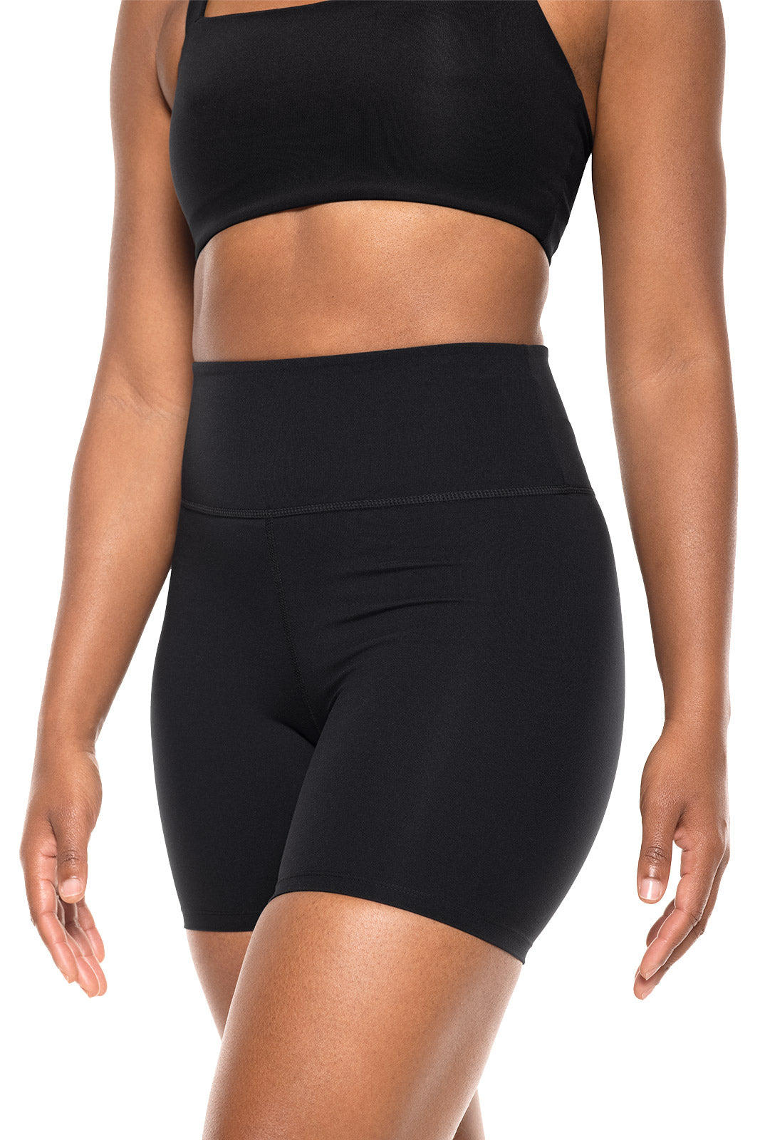 Person wearing a black sports bra and high-waisted black shorts on a white background