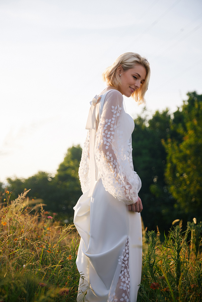 Woman in a white dress with floral details standing in a field.