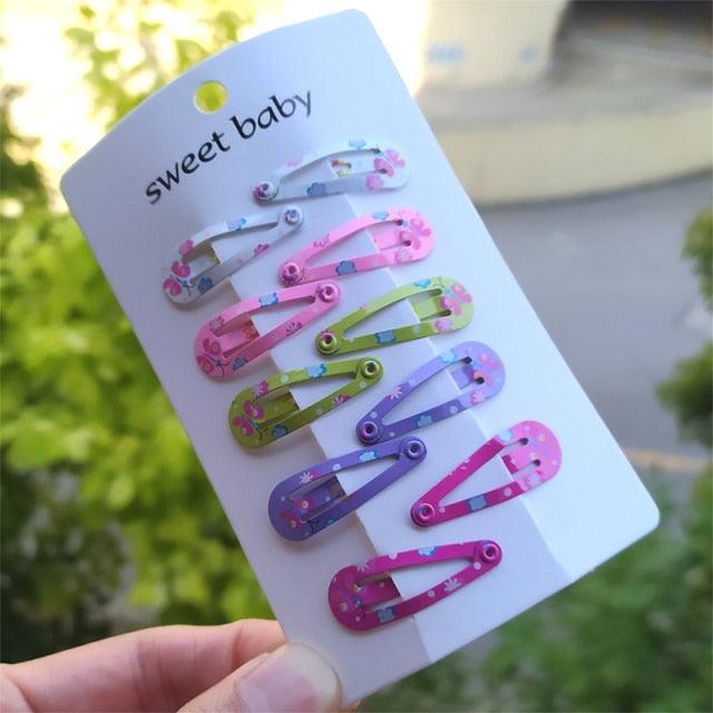 Set of colorful hair clips on a 'sweet baby' branded card held by a hand with a blurred green outdoor background.