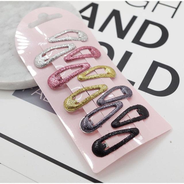 Set of colorful glittery hair clips on a pink card with 'HAND AND WORLD' text in the background.