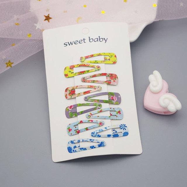 Colorful floral hair clips on a 'sweet baby' branded card with a pink toy in the background.