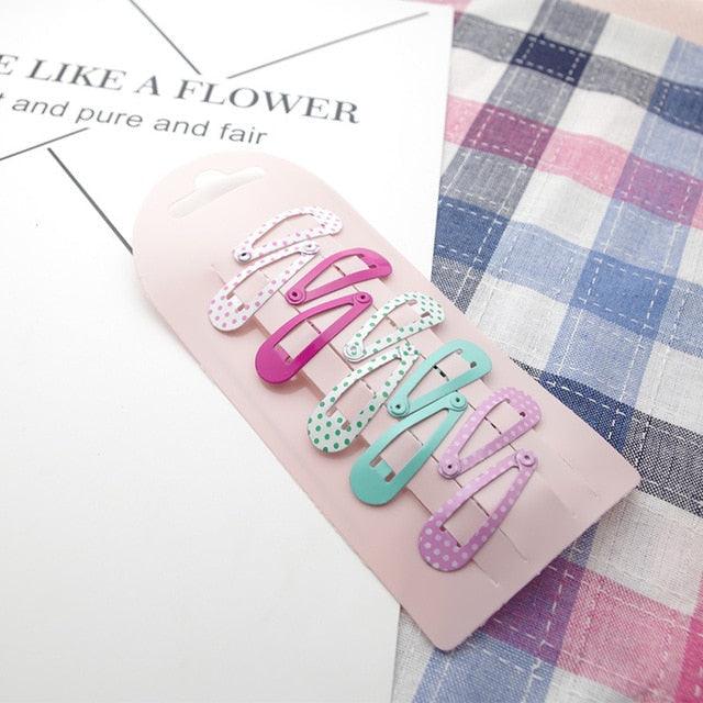 Set of colorful hair clips on a pink card with text and plaid fabric background