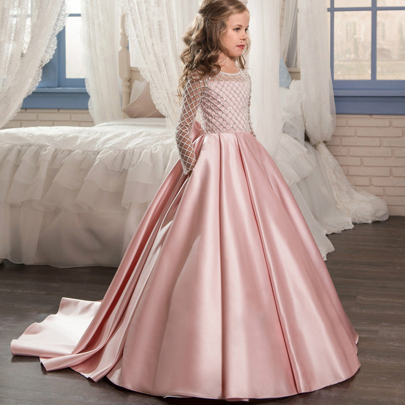 Young girl in a pink and white dress standing in a room with white curtains and a bed.