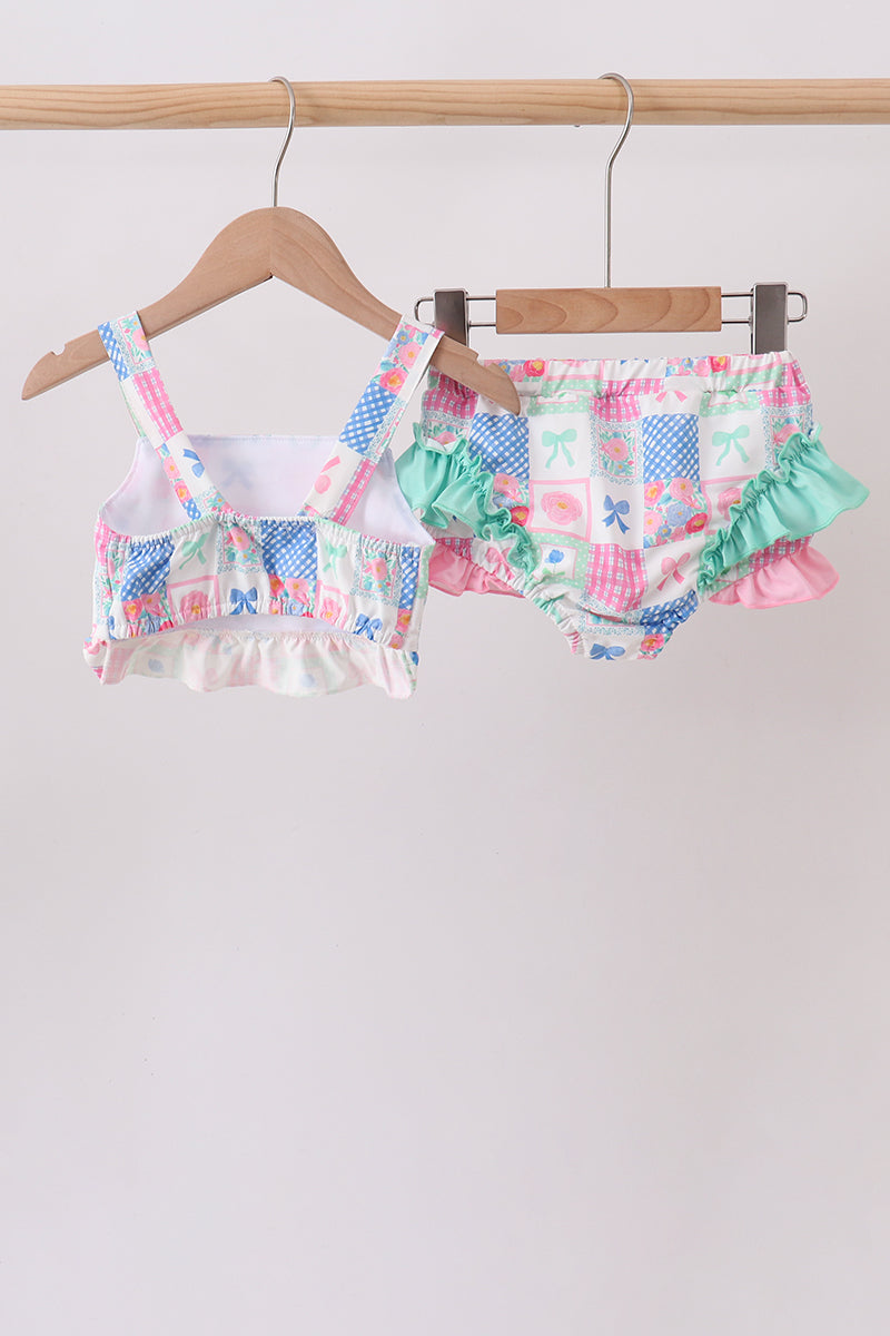 Colorful children's swimsuit with ruffles on a wooden hanger against a light gray background