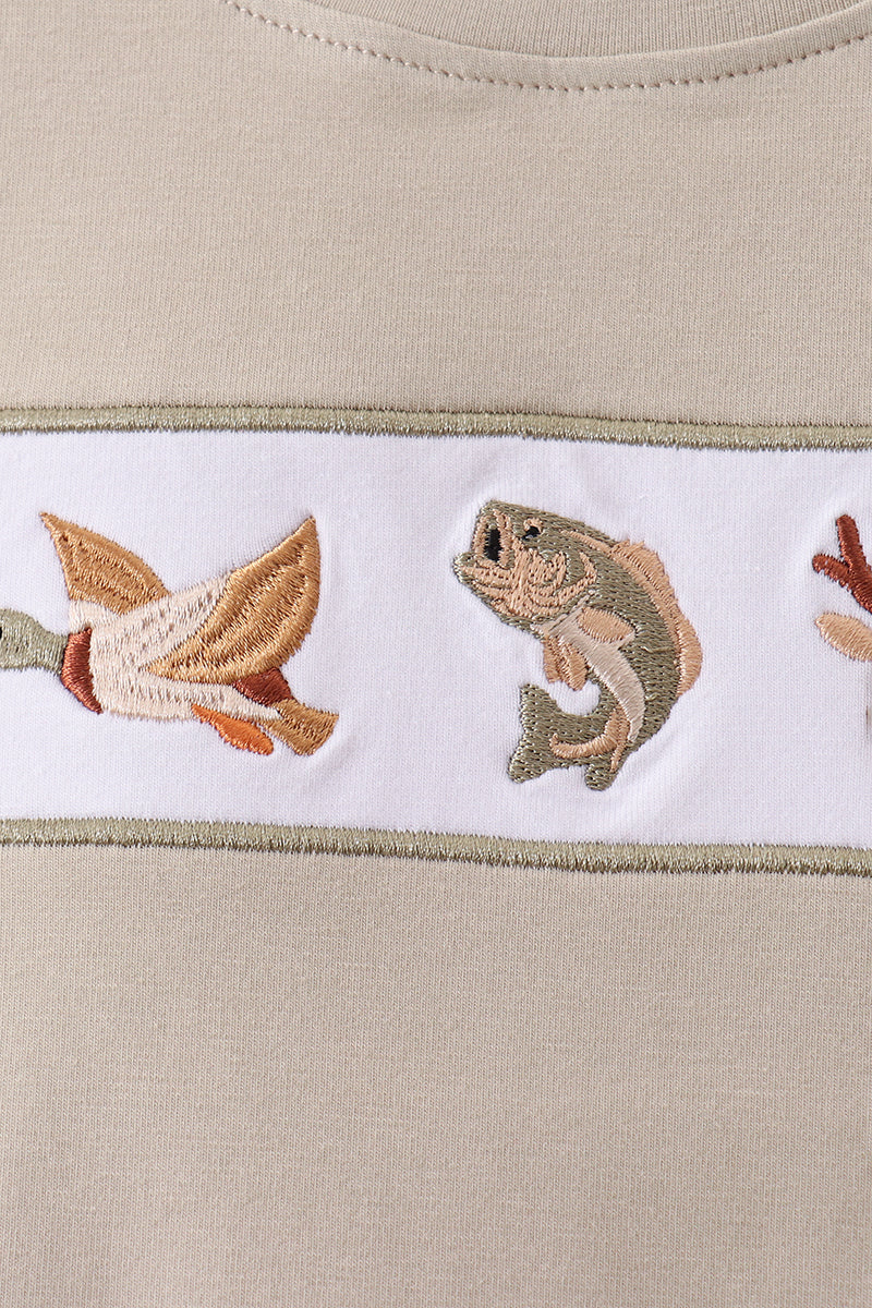 Close-up of a beige knit garment with a horizontal white embroidered band featuring a duck, a fish, and part of a bird.