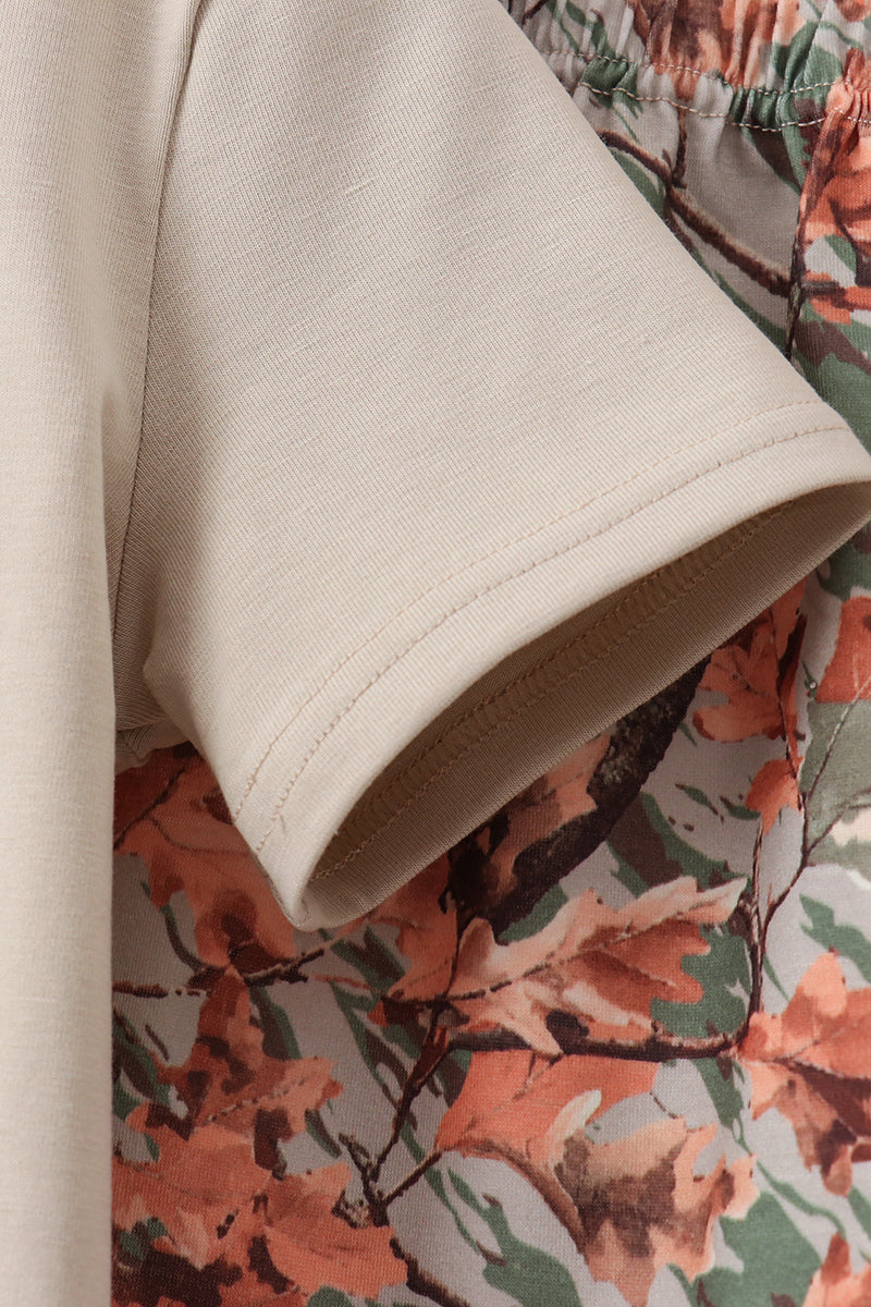 Close-up of a cream-colored short-sleeve t-shirt sleeve with a rolled cuff, layered over a green, brown, and orange autumn leaf patterned garment.