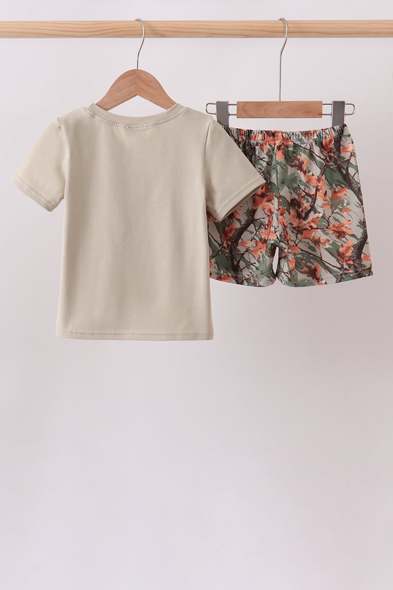 A two-piece children's outfit hanging on wooden hangers from a light wood rod. The set includes a short-sleeve crewneck t-shirt in a solid light beige color, and matching shorts with a dense floral print featuring orange, red, green, and brown tones.