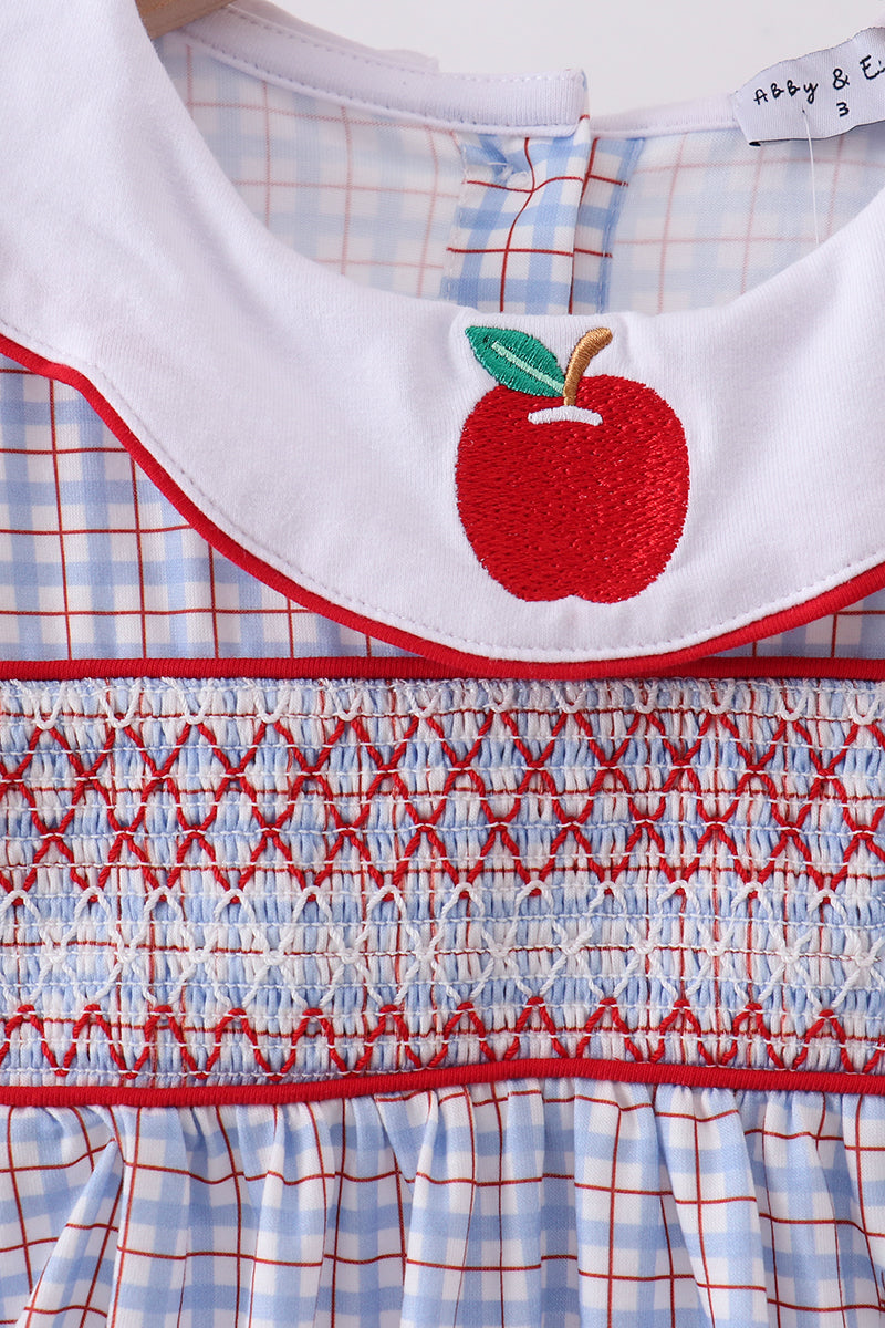 Close-up of a children's dress with a white Peter Pan collar featuring a red embroidered apple with green leaves, a smocked blue-and-white gingham bodice with red trim, and a blue-and-white gingham skirt.