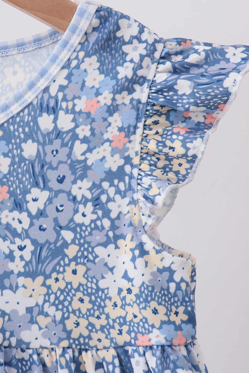 Close-up of a children's dress with a blue floral print, featuring flutter sleeves and a ruffled neckline, shown on a wooden hanger against a light gray background.