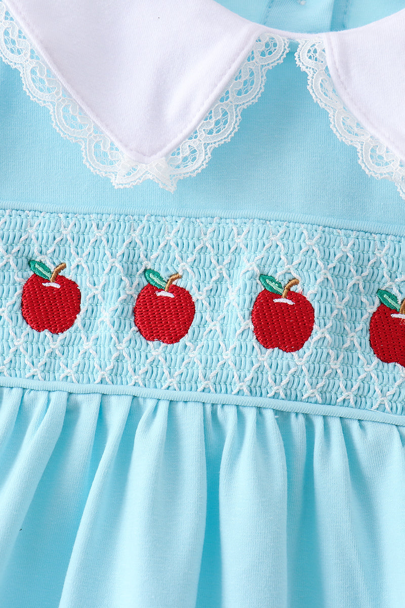 Close-up of a light blue dress with a white lace Peter Pan collar and embroidered red apples across a smocked chest panel.