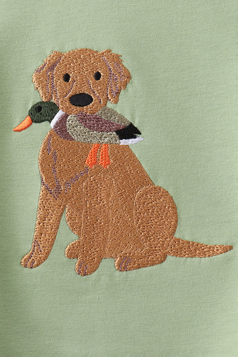 An embroidered design of a golden retriever dog holding a duck in its mouth, stitched on a light sage green fabric background.