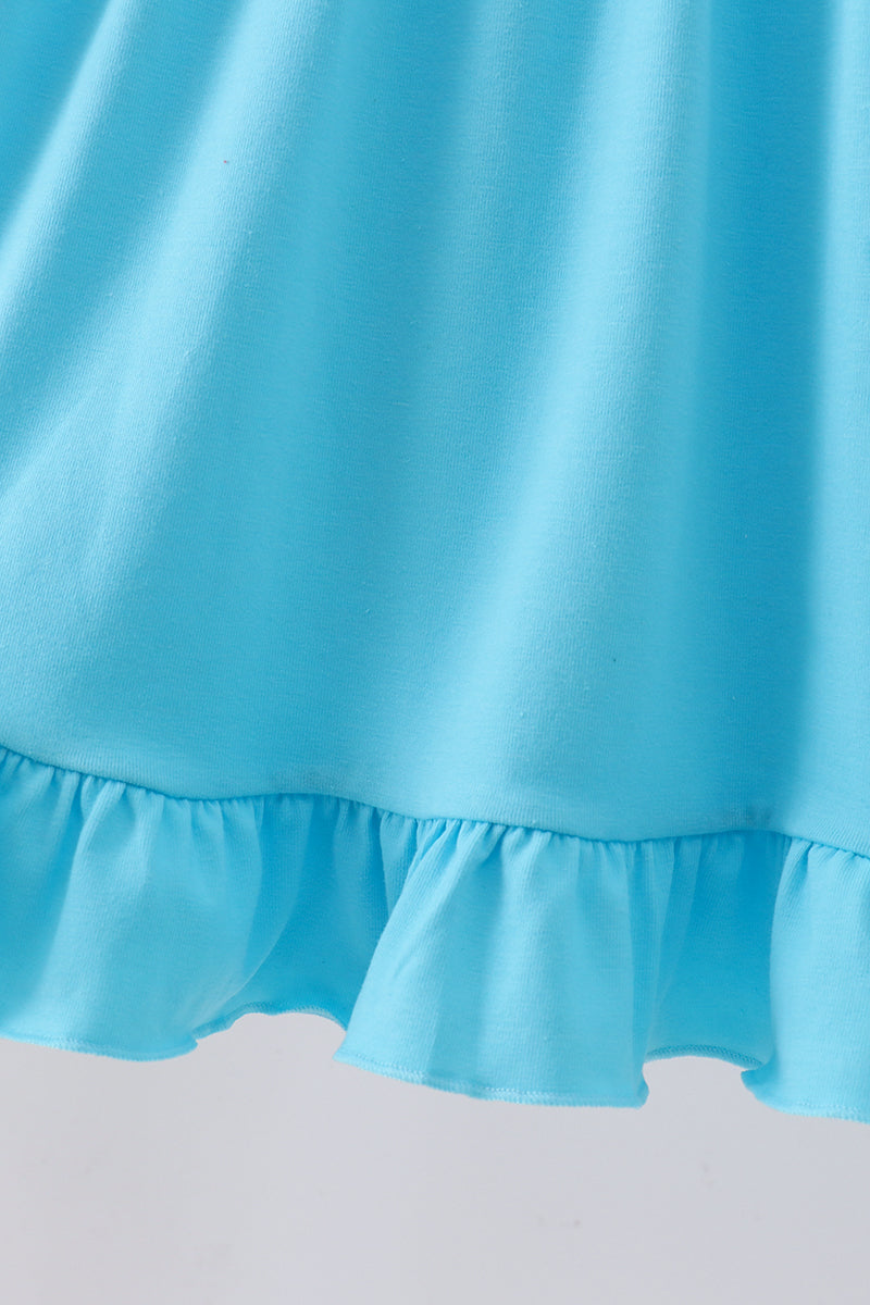 A close-up of a light blue fabric garment with a ruffled hem against a plain light background.