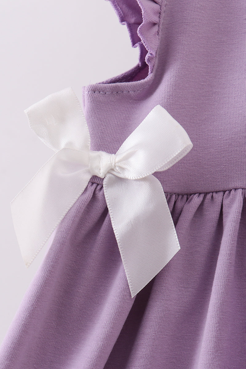 Close-up of a lavender purple dress with a large white satin bow at the waist and ruffled neckline details.