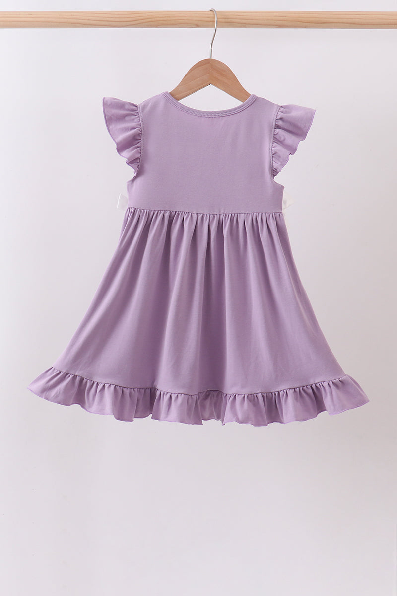 A lavender purple toddler girl's dress with ruffled cap sleeves and a ruffled hem, hanging on a wooden hanger against a plain white wall.