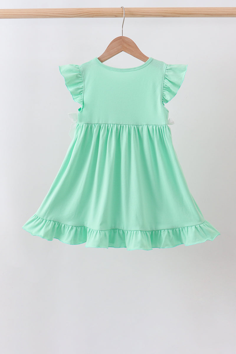 A mint green toddler girl's dress with ruffled cap sleeves and a tiered skirt, hanging on a wooden hanger against a plain white wall.