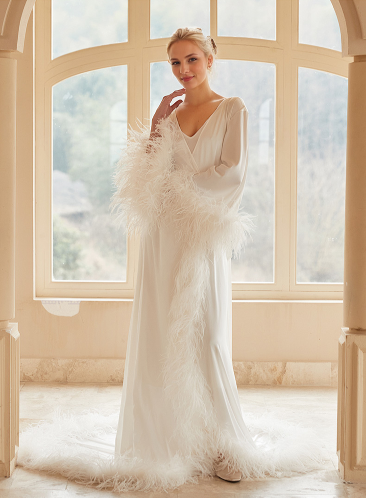 Woman in a white wedding dress standing in front of large windows with a soft, blurred background.