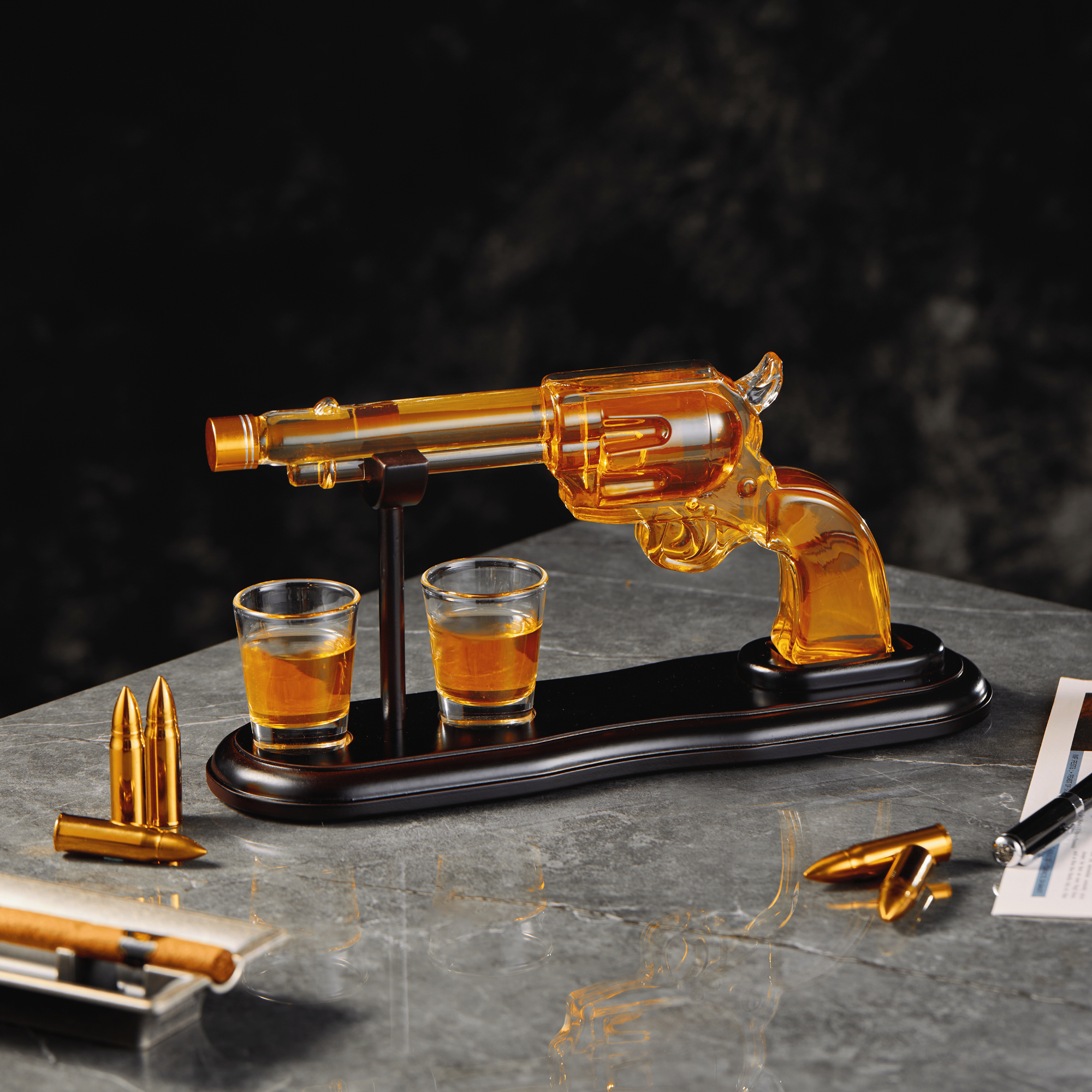 Glass gun-shaped decanter with two shot glasses on a dark surface