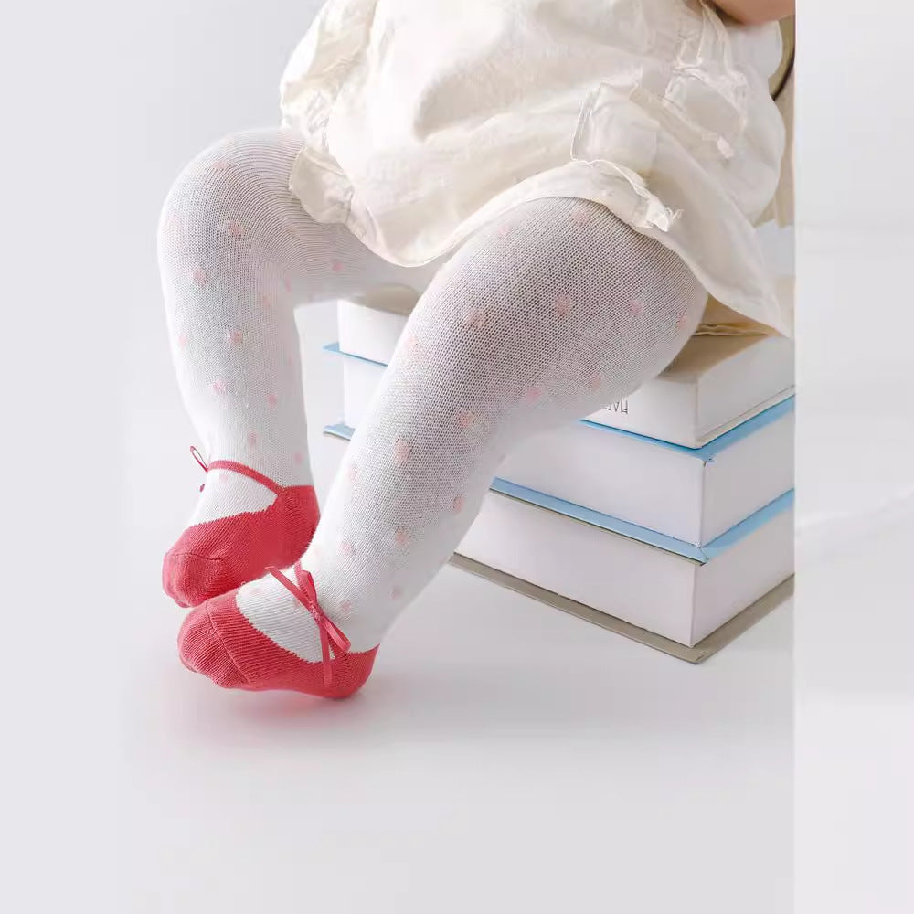 Child wearing white tights with pink shoes sitting on books against a light background