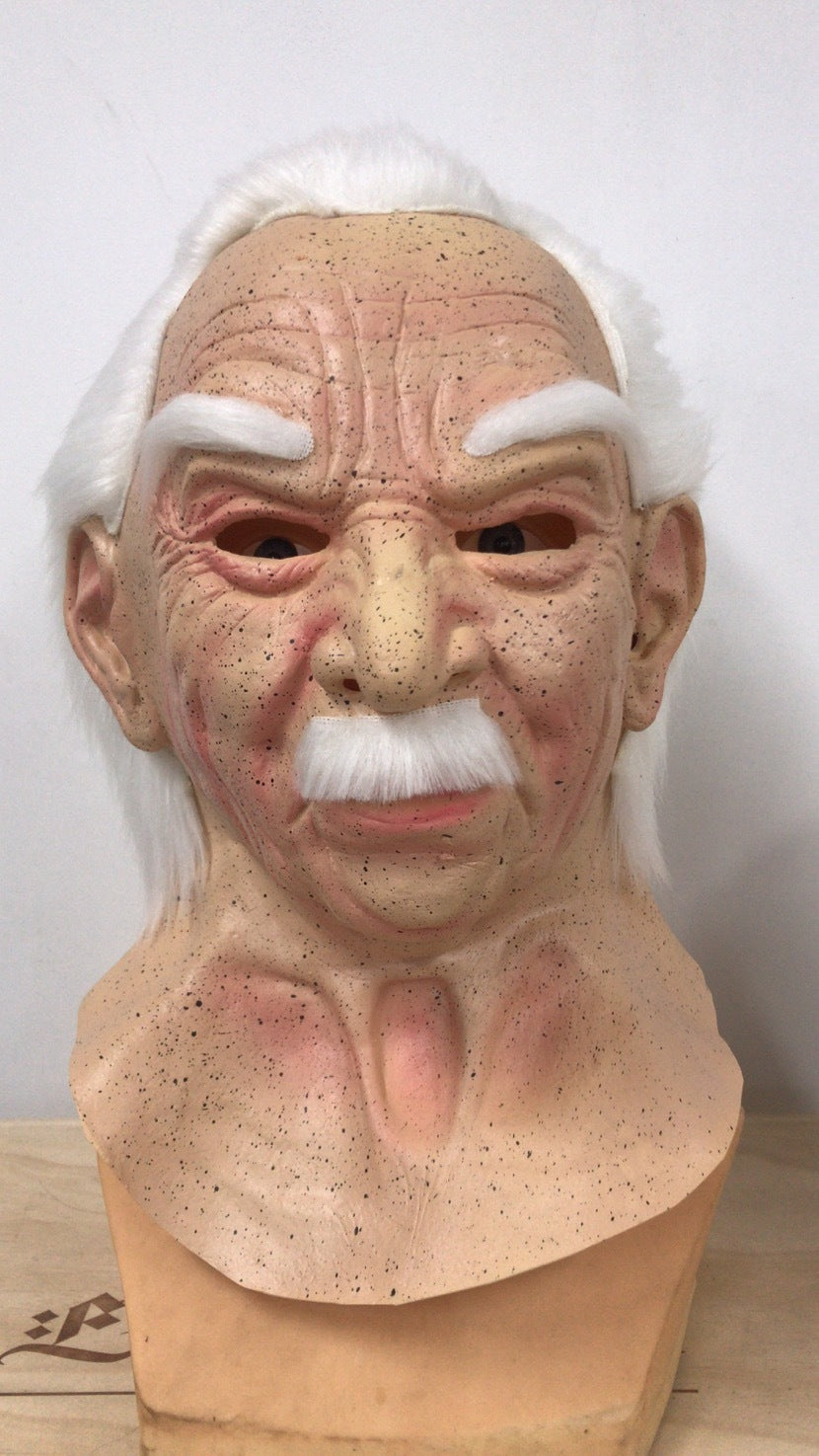 A realistic latex mask of an elderly man with white hair, white mustache, and a wrinkled face, displayed on a wooden stand against a plain light background.