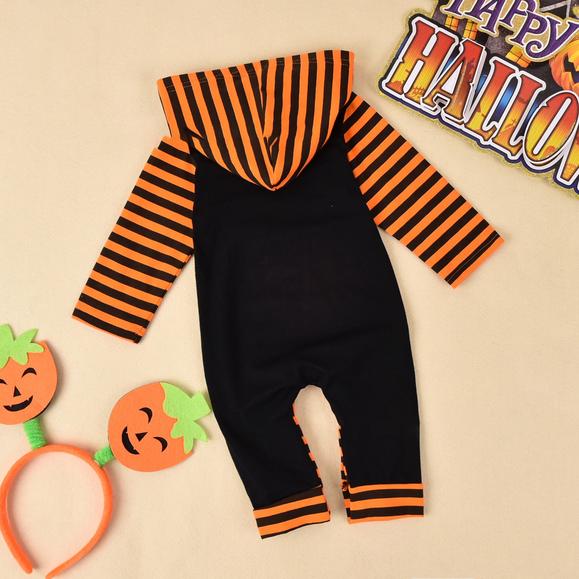 Black and orange striped baby romper with Halloween decorations on a beige background