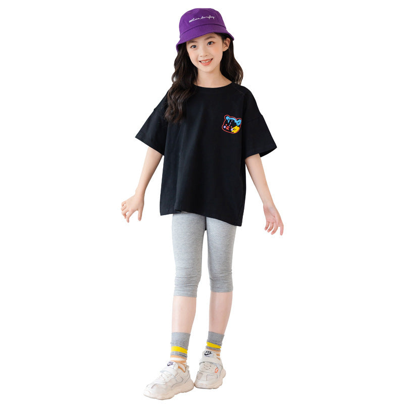 Child wearing a black t-shirt with a colorful design, gray leggings, and a purple cap on a white background