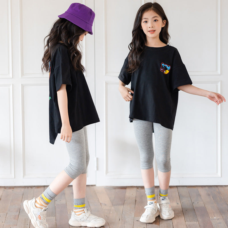 Two children wearing black t-shirts, gray leggings, and white sneakers on a wooden floor.