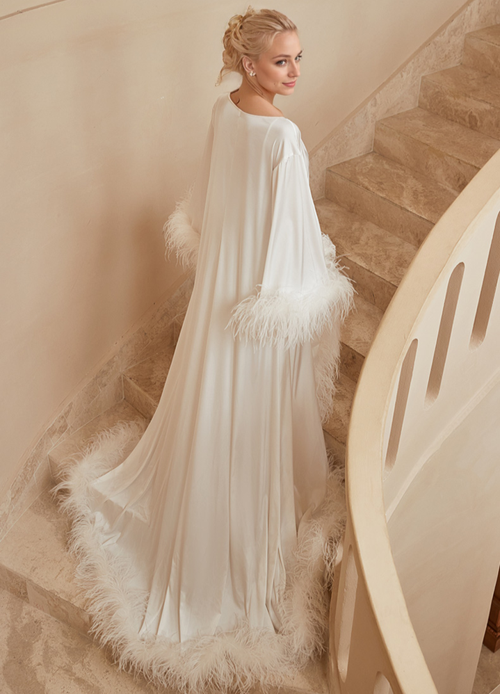 Woman in a white gown with feathered details standing on a staircase.