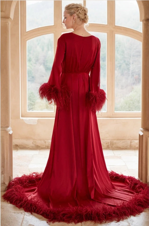 Woman wearing a red evening gown with feathered sleeves and skirt in a room with large windows.