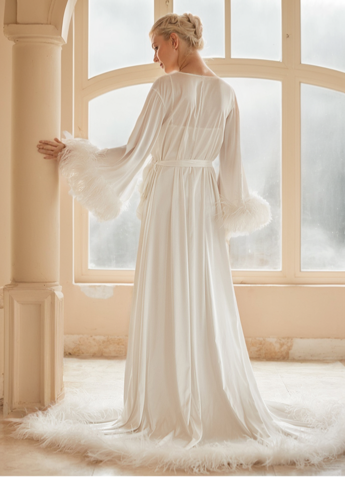 Woman in a long, flowing white dress standing in a room with large windows.