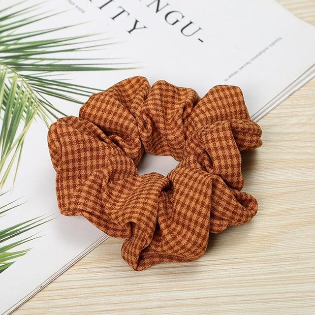 Brown checkered scrunchie on a magazine with green leaves