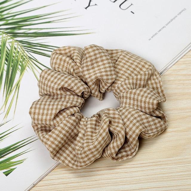 Brown checkered scrunchie on a light wooden surface with green leaves.