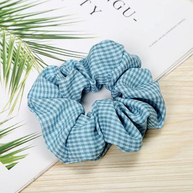 Blue and white checkered scrunchie on a wooden surface with green leaves in the background