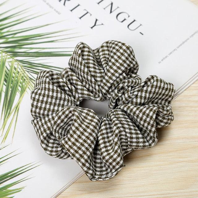 Checkered scrunchie on a surface with text and green leaves in the background