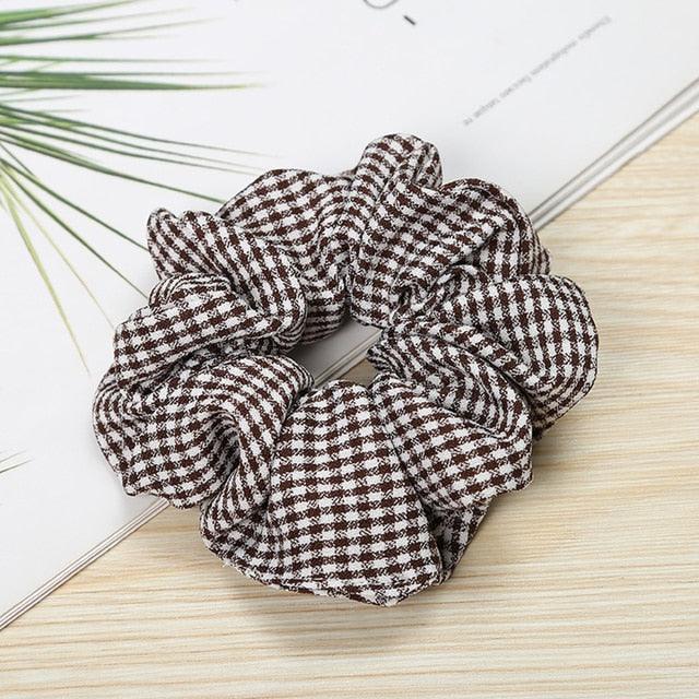 Brown and white checkered scrunchie on a light wooden surface with a plant in the background