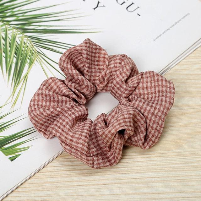 Plaid scrunchie on a wooden surface with green leaves