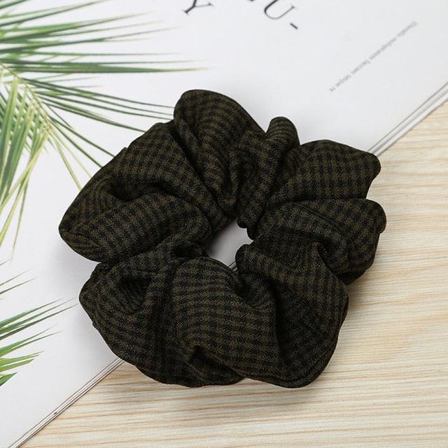 Dark green scrunchie on a light wooden surface with a white paper background