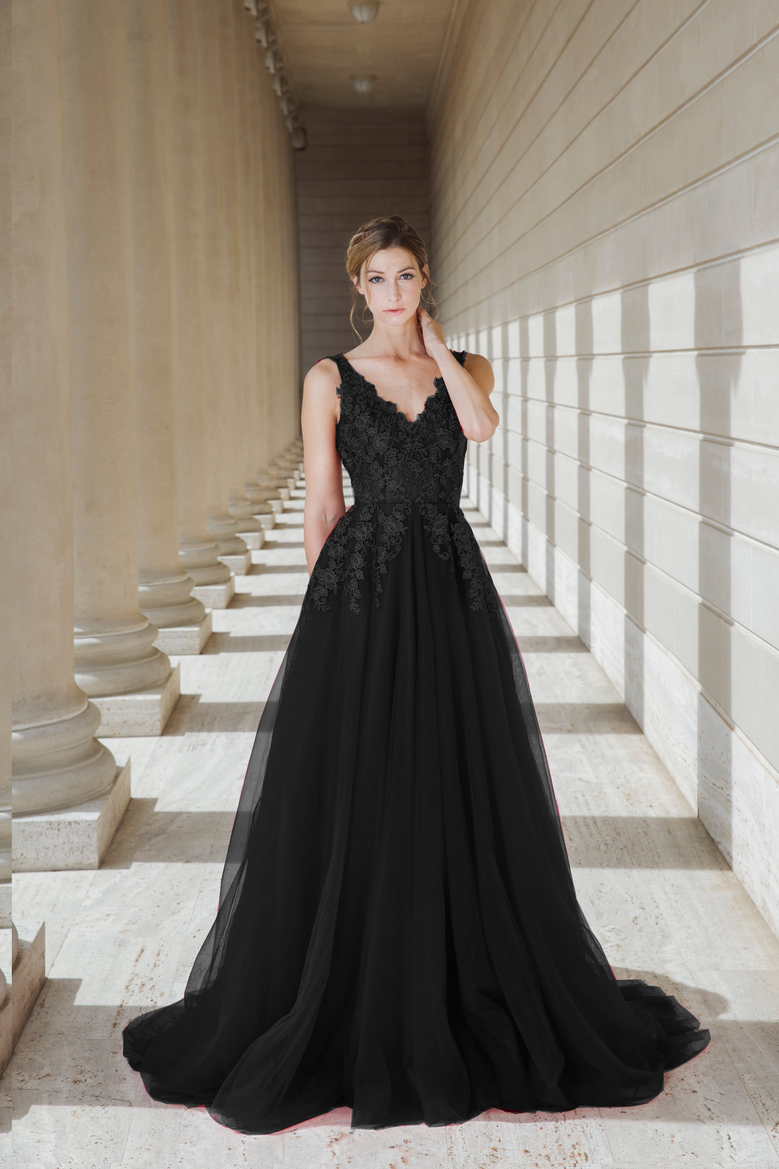 Woman in a black evening gown standing in a sunlit hallway with columns.